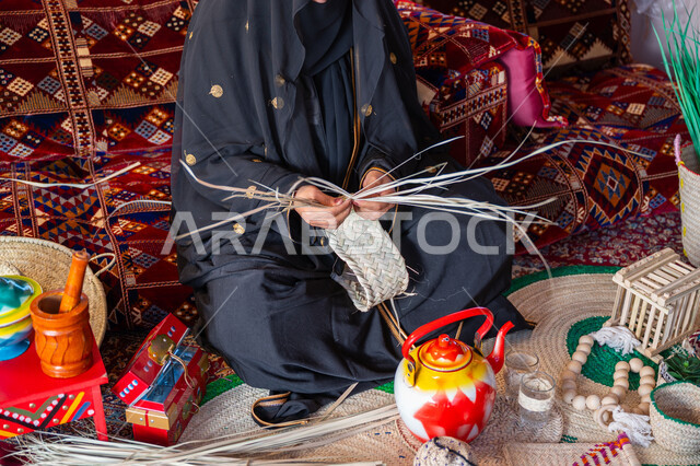 ارتداء الزي الشعبي في المناسبة الوطنية، استخدام أوراق النخيل المجففة في صناعة السلل، حرفة يدوية تقليدية, ذكرى تأسيس الدولة السعودية الأولى في 1727م، صورة مقربة لامرأة عربية خليجية سعودية ترتدي العباءة تجلس في خيمة في الصحراء تقوم بجدل سعائف الخوص, يوم بدينا 22 فبراير