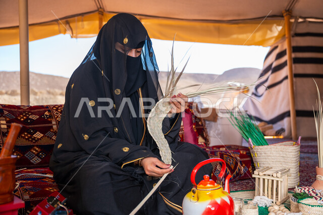 حرفة يدوية تقليدية, ذكرى تأسيس الدولة السعودية الأولى في 1727م، امرأة عربية خليجية سعودية ترتدي النقاب والعباءة تجلس في خيمة في الصحراء تقوم بجدل سعائف الخوص, ارتداء الزي الشعبي في المناسبة الوطنية، يوم بدينا 22 فبراير، استخدام أوراق النخيل المجففة في صناعة السلل