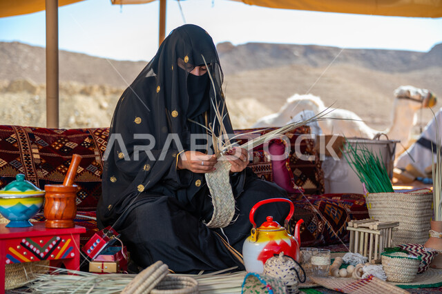 حرفة يدوية تقليدية, ذكرى تأسيس الدولة السعودية الأولى في 1727م، امرأة عربية خليجية سعودية ترتدي النقاب والعباءة تجلس في خيمة في الصحراء تقوم بجدل سعائف الخوص, ارتداء الزي الشعبي في المناسبة الوطنية، يوم بدينا 22 فبراير، استخدام أوراق النخيل المجففة في صناعة السلل