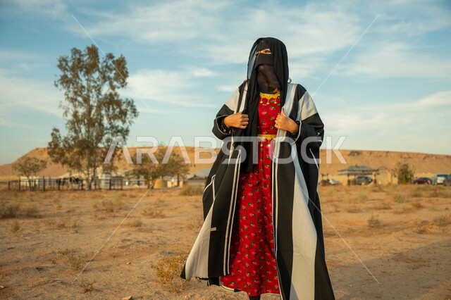 يوم بدينا 22 فبراير، الاهتمام والعناية بالمظهر الخارجي، ارتداء زي المنطقة الوسطى في المناسبة الوطنية، إمرأة خليجية عربية سعودية ترتدي البشت السعودي النسائي والبرقع تقف على الرمال الذهبية الناعمة في الصحراء، ذكرى تأسيس الدولة السعودية الأولى 1727 م، تعابير الفخر والثقة