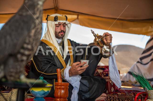 العادات الخليجية الأصيلة في كرم الضيافة، مكانة الصقر في التاريخ السعودي, ذكرى تأسيس الدوله السعوديه الأولى 1727م, يوم بدينا 22 فبراير، رجل عربي خليجي سعودي يرتدي العقال الذهبي العريض والغترة والبشت يجلس داخل الخيمة ويقوم بصب فنجان من القهوة العربية