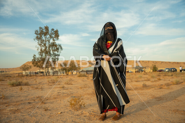 ذكرى تأسيس الدولة السعودية الأولى 1727 م، ارتداء زي المنطقة الوسطى في المناسبة الوطنية، الاهتمام والعناية بالمظهر الخارجي، إمرأة خليجية عربية سعودية ترتدي البشت النسائي السعودي والبرقع تقف على الرمال الذهبية الناعمة في الصحراء، يوم بدينا 22 فبراير