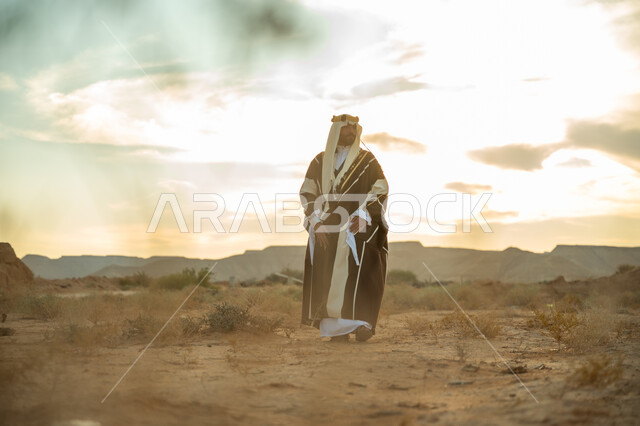 The concept of patriotism and belonging to the country, a popular national occasion, showing loyalty and devotion to the country, the anniversary of the founding of the first Saudi state 1727 AD, the day we started February 22, a Saudi Gulf Arab man wearing a ghutra and a bisht walking in the desert and looking at something, a desert background