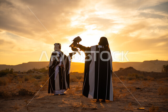 رمز القوة والتحدي وحدة البصر, اهمية الصقور في التاريخ السعودي, ذكرى تأسيس الدوله السعوديه الاولى 1727 م, يوم بدينا 22 فبراير، غروب الشمس في الصحراء, توارث شغف تربية الجوارح, رجل وامرأة عربيان خليجيان سعوديان يرتديان الزي الشعبي ويحملان طائر الصقر