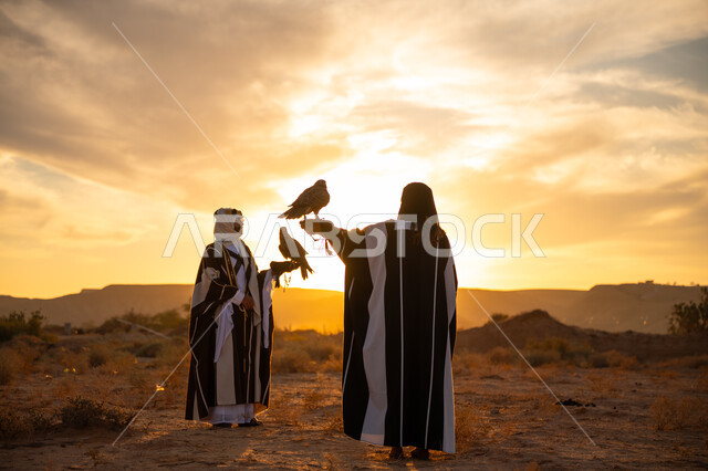 يوم بدينا 22 فبراير، غروب الشمس في الصحراء, توارث شغف تربية الجوارح, رمز القوة والتحدي وحدة البصر, اهمية الصقور في التاريخ السعودي, ذكرى تأسيس الدوله السعوديه الاولى 1727 م, رجل وامرأة عربيان خليجيان سعوديان يرتديان الزي الشعبي ويحملان طائر الصقر
