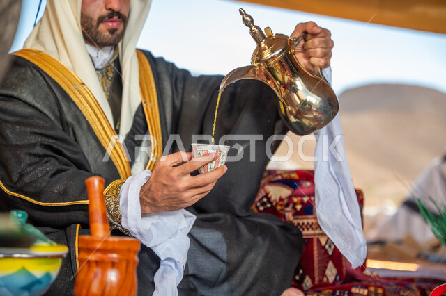 الفخر بتراث الأجداد, التقاليد والعادات العربية و كرم الضيافة، الاحتفال بعيد ومناسبة وطنية, يوم بدينا 1727م، ارتداء الزي الشعبي في يوم تأسيس الدولة السعودية الأولى 22 فبراير, صورة مقربة ليدي رجل عربي خليجي سعودي يرتدي البشت والغترة يقوم بصب فنجان من القهوة