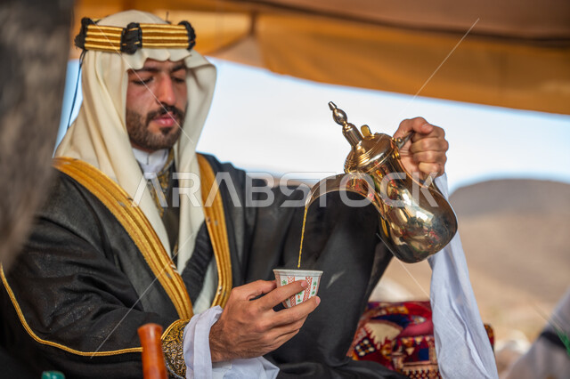 يوم بدينا 1727 م، الشموخ والاعتزاز والفخر, الاحتفال بعيد ومناسبة وطنية, ارتداء الزي الشعبي في يوم تأسيس الدولة السعودية الأولى 22 فبراير, رجل عربي خليجي سعودي يرتدي البشت والغترة والعقال الذهبي العريض يقوم بصب فنجان من القهوة, اتباع التقاليد في كرم الضيافة