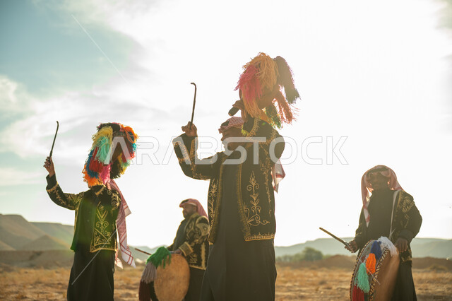 A men's folklore band performing in one of the desert regions of the Kingdom, wearing embroidered traditional clothing and the shemagh on a national occasion, the day of our beginning, February 22, the anniversary of the founding of the first Saudi state in 1727 AD, celebrating the National Day by beating the drum decorated with colored threads, chants and traditional dancing