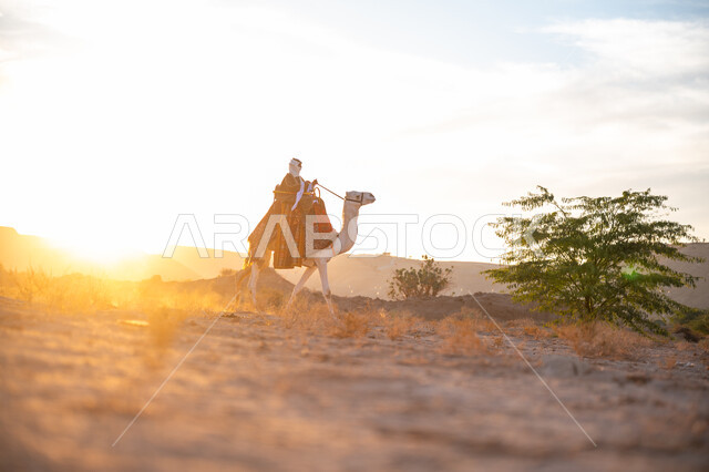 ذكرى تأسيس الدولة السعودية الأولى 1727م, الاعتزاز والفخر بالانتماء للوطن, يوم بدينا 22 فبراير, ارتداء الزي الشعبي في المناسبة الوطنية, صورة من الجانب لرجل عربي خليجي سعودي يرتدي البشت التقليدي والغترة يمتطي الجمل وسط الصحراء في وقت غروب الشمس