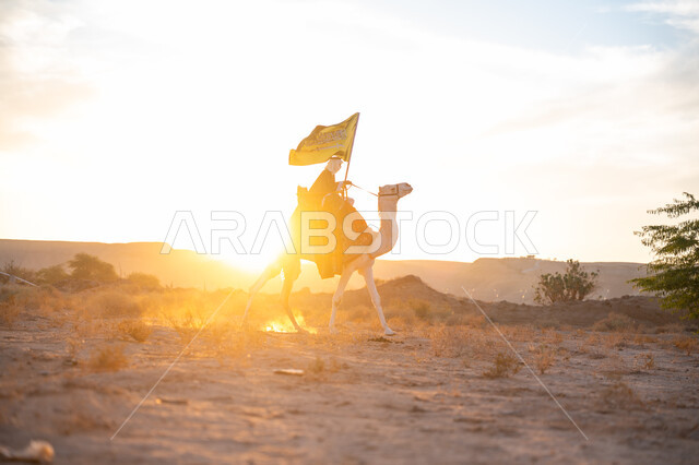 ارتباط الإبل بالأصالة والعراقة, ارتداء الزي الشعبي في المناسبة الوطنية، يوم بدينا 22 فبراير, صورة من الجانب لرجل عربي خليجي سعودي يرتدي البشت التقليدي والغترة يمتطي الجمل وسط الصحراء ويحمل علم المملكة وقت غروب الشمس, ذكرى تأسيس الدولة السعودية الأولى  1727م