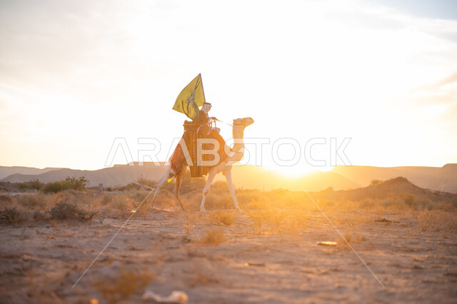 يوم بدينا 22 فبراير, صورة من الجانب لرجل عربي خليجي سعودي يرتدي البشت التقليدي والغترة يمتطي الجمل وسط الصحراء ويحمل علم المملكة وقت غروب الشمس, ذكرى تأسيس الدولة السعودية الأولى  1727م, ارتباط الإبل بالأصالة والعراقة, ارتداء الزي الشعبي في المناسبة الوطنية