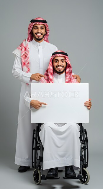 موك اب مربع أبيض، استخدام وسيلة تعليمية وتوضيحية، إعلان وعرض تسويقي، بورتريه لشاب عربي خليجي سعودي مبتسم يرتدي الثوب التقليدي والشماغ يقف بجانب صديقه المقعد يجلس على كرسي متحرك يحمل بيده لوحة بيضاء فارغة يشيران إليها بإصبع السبابة، خلفية رمادية