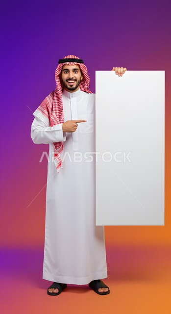 إعلان وعرض تسويقي، استخدام لوحة توضيحية ووسيلة تعليمية، موك اب مربع أبيض، بورتريه لشاب عربي خليجي سعودي مبتسم يرتدي الثوب التقليدي والشماغ يشير بإصبع السبابة إلى لوحه بيضاء مربعه فارغة ينظر إلى الكاميرا بإيماءات السرور، صورة الجسم بالطول الكامل، خلفية ملونة