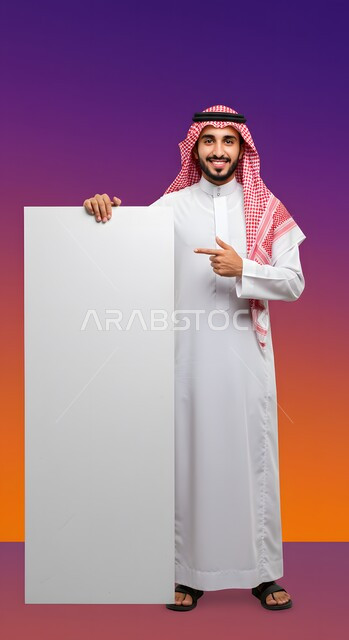 موك اب مربع أبيض، إعلان وعرض تسويقي، استخدام لوحة توضيحية ووسيلة تعليمية، بورتريه لشاب عربي خليجي سعودي مبتسم يرتدي الثوب التقليدي والشماغ يشير بإصبع السبابة إلى لوحه بيضاء مربعه فارغة ينظر إلى الكاميرا بإيماءات السرور، صورة الجسم بالطول الكامل، خلفية ملونة
