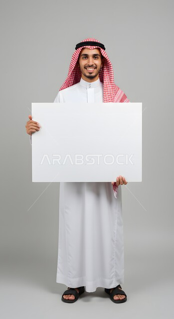 عرض وإعلان تسويقي، موك اب مربع أبيض، استخدام لوحة توضيحية ووسيلة تعليمية، بورتريه لشاب عربي خليجي سعودي مبتسم يرتدي الثوب التقليدي والشماغ يحمل بيده لوحه بيضاء مربعه فارغة ينظر إلى الكاميرا بإيماءات السرور، صورة الجسم بالطول الكامل، خلفية ملونة