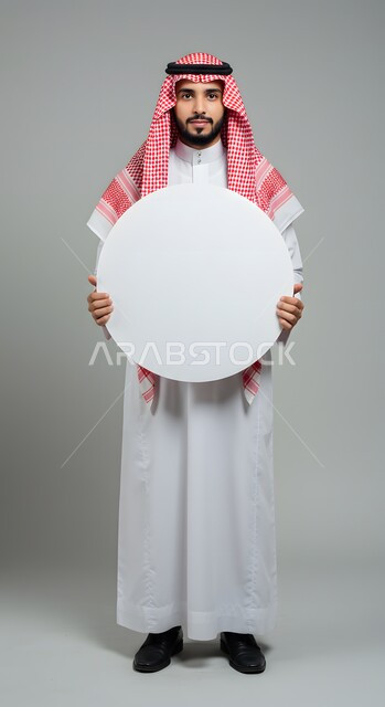 عرض و إعلان تسويقي، موك اب دائري أبيض، استخدام لوحة توضيحية ووسيلة تعليمية، بورتريه لشاب عربي خليجي سعودي يرتدي الثوب التقليدي والشماغ يحمل بيده لوحه بيضاء مدورة فارغة ينظر إلى الكاميرا بإيماءات الثقة بالنفس، صورة الجسم بالطول الكامل، خلفية ملونة