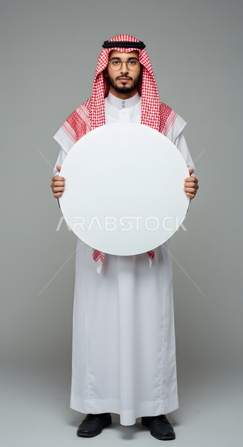 موك اب دائري أبيض، استخدام لوحة توضيحية ووسيلة تعليمية، عرض و إعلان تسويقي، بورتريه لشاب عربي خليجي سعودي يرتدي الثوب التقليدي والشماغ والنظارة الطبية يحمل بيده لوحه بيضاء مدورة فارغة ينظر إلى الكاميرا بإيماءات الثقة بالنفس، صورة الجسم بالطول الكامل، خلفية ملونة