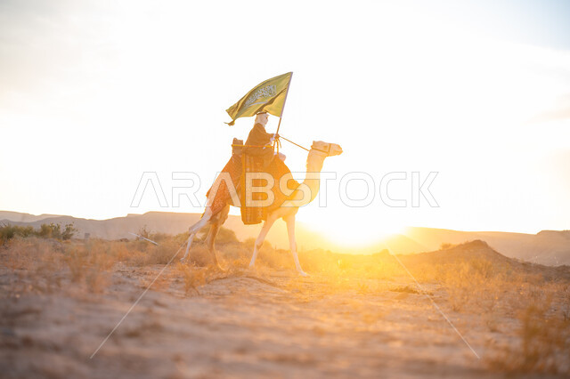 ذكرى تأسيس الدولة السعودية الأولى  1727م, ارتباط الإبل بالأصالة والعراقة, ارتداء الزي الشعبي في المناسبة الوطنية, رجل عربي خليجي سعودي يرتدي البشت والغترة يمتطي الجمل في الصحراء ويحمل علم المملكة وقت غروب الشمس, الفخر بالإنتماء الى الوطن, يوم بدينا 22 فبراير