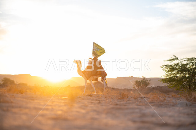 ارتباط الإبل بالأصالة والعراقة, ارتداء الزي الشعبي في المناسبة الوطنية, رجل عربي خليجي سعودي يرتدي البشت والغترة يمتطي الجمل في الصحراء ويحمل علم المملكة وقت غروب الشمس, الفخر بالإنتماء الى الوطن, يوم بدينا 22 فبراير, ذكرى تأسيس الدولة السعودية الأولى  1727م