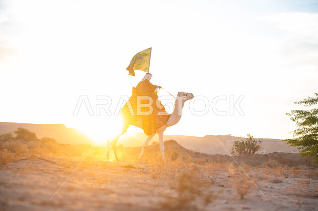 The day we started is February 22, wearing the traditional costume on the founding day of the first Saudi state in 1727 AD, celebrating a national holiday and occasion, pride and honor in belonging to the homeland, a Saudi Gulf Arab man wearing a bisht and a ghutra riding a camel in the desert and carrying the flag of the Kingdom at sunset