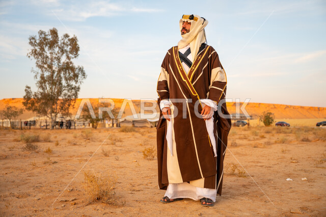 يوم بدينا 22 فبراير, مفهوم حب الوطن والانتماء اليه, ارتداء الزي الشعبي في مناسبة وطنية, ذكرى تأسيس الدولة السعودية الأولى 1727م, رجل عربي خليجي سعودي يرتدي البشت التقليدي والعقال الذهبي يقف على الرمال الذهبية في الصحراء