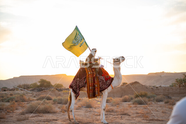 ذكرى تأسيس الدولة السعودية الأولى 1727م, يوم بدينا 22 فبراير, رجل عربي خليجي سعودي يرتدي البشت والغترة يمتطي الجمل في الصحراء ويحمل علم المملكة, راية الإسلام والتوحيد, ارتداء الزي الشعبي التقليدي في مناسبة وطنية, مفهوم حب الوطن والانتماء اليه