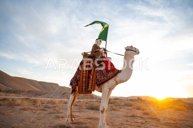 ارتداء الزي الشعبي في المناسبة الوطنية, يوم بدينا 22 فبراير, ذكرى تأسيس الدولة السعودية الأولى في 1727م, رجل عرب خليجي سعودي يرتدي البشت والغترة يمتطي الجمل في الصحراء ويحمل علم المملكة في وقت غروب الشمس, راية الإسلام والتوحيد, يوم العلم 11 مارس