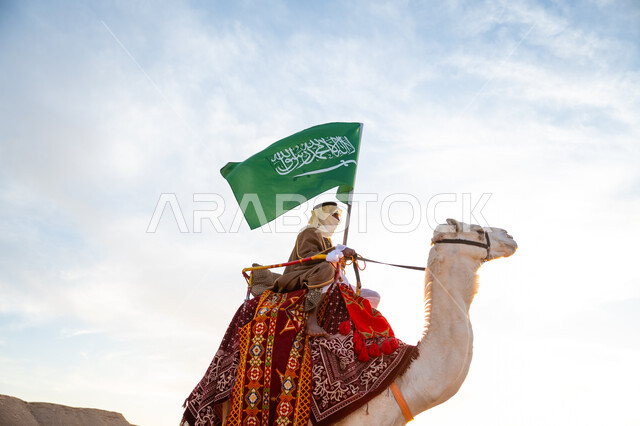 ذكرى تأسيس الدولة السعودية الأولى في 1727م, يوم بدينا 22 فبراير، ارتداء الزي الشعبي في المناسبة الوطنية, رجل عرب خليجي سعودي يرتدي البشت والغترة يمتطي الجمل في الصحراء ويحمل علم المملكة, راية الإسلام والتوحيد, يوم العلم 11 مارس