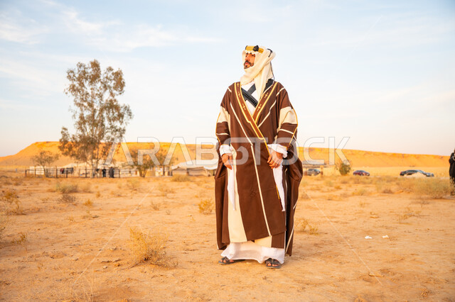 The concept of patriotism and belonging to the homeland, the day we started on February 22, wearing traditional folk costume on a national occasion, the anniversary of the founding of the first Saudi state 1727 AD, a Saudi Gulf Arab man wearing the traditional bisht and golden headband standing on the golden sands of the desert
