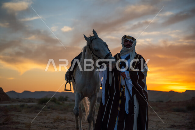 الرعاية والاهتمام بالخيول, ذكرى تأسيس الدولة السعودية الأولى 1727م, رجل عربي خليجي سعودي يرتدي البشت والعقال الذهبي يقف مع حصانه الأصيل في الصحراء بوقت غروب الشمس, توارث حب الجياد من الأجداد, يوم بدينا 22 فبراير, ارتداء الزي الشعبي التقليدي في مناسبة وطنية
