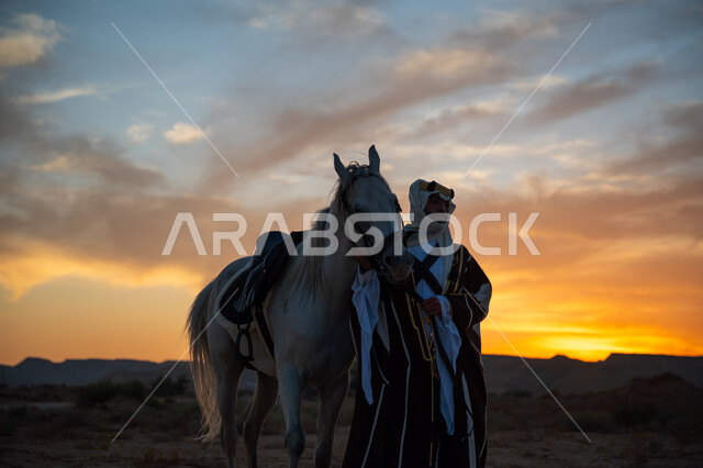 ذكرى تأسيس الدولة السعودية الأولى 1727م, الرعاية والاهتمام بالخيول, رجل عربي خليجي سعودي يرتدي البشت والعقال الذهبي يقف مع حصانه الأصيل في الصحراء بوقت غروب الشمس, توارث حب الجياد من الأجداد, يوم بدينا 22 فبراير, ارتداء الزي الشعبي التقليدي في مناسبة وطنية