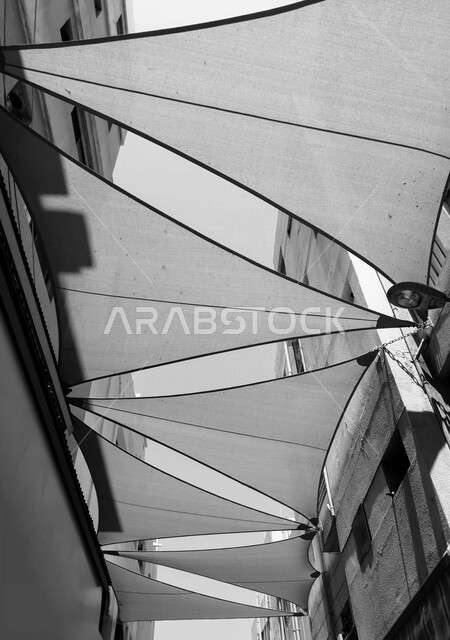 صورة لأشرعة على السقف بين المباني , مظلات قماشية تحمي من أشعة الشمس , تصاميم تشبه الشراع تعطي ظل للمكان .