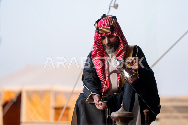 مناسبة و احتفال وطني, ذكرى تاسيس الدوله السعوديه الاولى 1727م, يوم بدينا 22 فبراير، رجل عربي خليجي سعودي يرتدي البشت و الشماغ التقليدي يقوم بصب القهوة في خيمة شعبية في الصحراء في النهار، مفهوم حسن الضيافة والاستقبال عند العرب