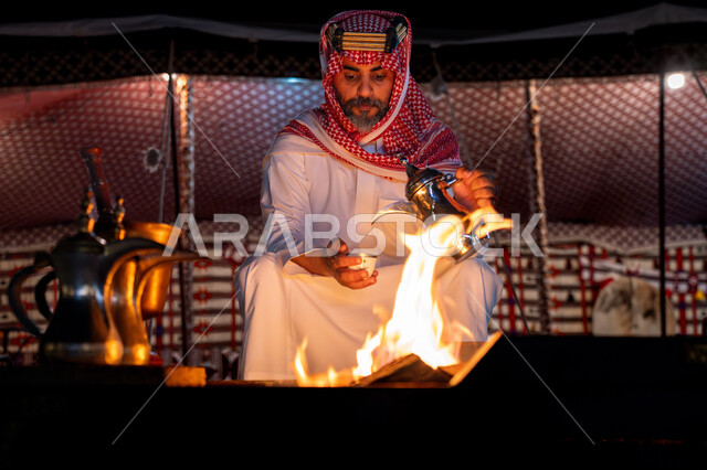 مفهوم حسن الضيافة والاستقبال عند العرب, احتفال و مناسبة وطنية, اجواء شتوية ليلية, يوم بدينا 22 فبراير، ذكرى تاسيس الدوله السعوديه الاولى 1727م, رجل عربي خليجي سعودي يرتدي الشماغ و الثوب التقليدي يقوم بصب القهوة, خيمة شعبية في الصحراء