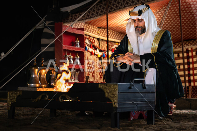 A popular tent in the desert, the day we started, February 22, the anniversary of the founding of the first Saudi state, 1727 AD, a Saudi Gulf Arab man wearing the traditional bisht and shemagh sitting in front of a fire, a winter night atmosphere, a national occasion and celebration