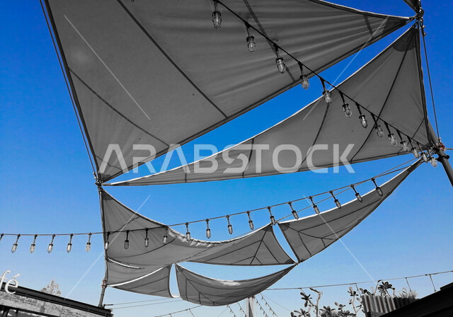 صورة لأشرعة على السقف بين المباني , مظلات قماشية تحمي من أشعة الشمس , تصاميم تشبه الشراع تعطي ظل للمكان .
