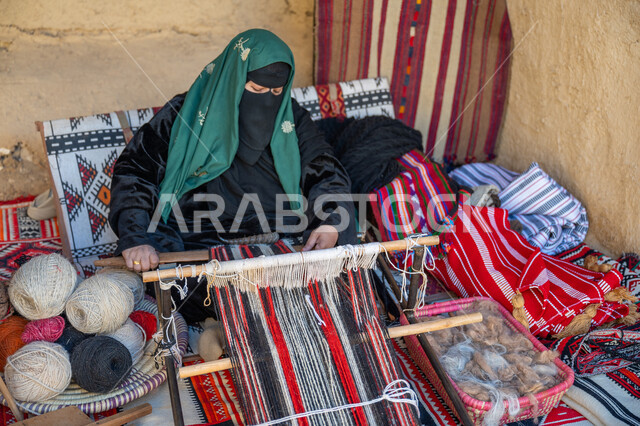 إحياء التراث الشعبي السعودي، يوم بدينا ٢٢ فبراير، حرفة ومهنة يدوية قديمة، صناعة تقليدية تاريخية، صورة من الاعلى لسيدة عربية خليجية سعودية ترتدي العباءة والبرقع تقوم بنسج وغزل الصوف، ذكرى تاسيس الدوله السعوديه الاولى ١٧٢٧م، منتج وطني محلي