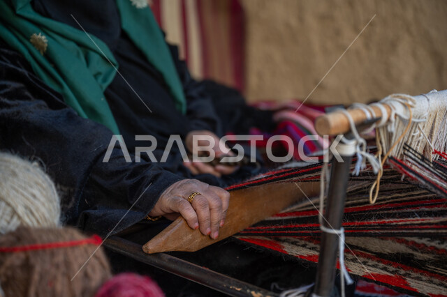 حرفة ومهنة يدوية قديمة، صناعة تقليدية تاريخية, ذكرى تاسيس الدوله السعوديه الاولى ١٧٢٧م، منتج وطني محلي, يوم بدينا ٢٢ فبراير، صورة مقربة لأيدي سيدة عربية خليجية سعودية ترتدي العباءة والبرقع تقوم بنسج وغزل الصوف، احياء التراث الشعبي السعودي