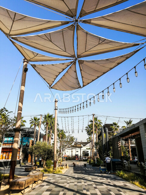 صورة لأشرعة على السقف بين المباني , مظلات قماشية تحمي من أشعة الشمس , تصاميم تشبه الشراع تعطي ظل للمكان .