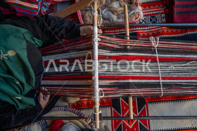 Local national product, historical traditional industry, anniversary of the founding of the first Saudi state 1727 AD, the day we started February 22, an ancient manual craft and profession, a picture from above of the hands of a Saudi Gulf Arab woman wearing an abaya and a burqa weaving and spinning wool, reviving the Saudi folk heritage