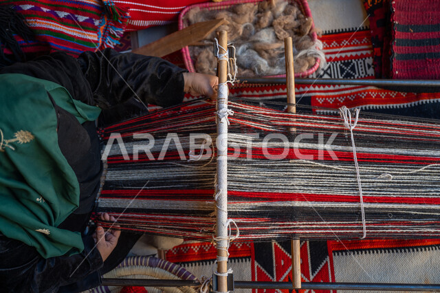 Historical traditional industry, the anniversary of the founding of the first Saudi state in 1727 AD, a local national product, the day we started is February 22, an ancient manual craft and profession, a picture from above of the hands of a Saudi Gulf Arab woman wearing an abaya and a burqa weaving and spinning wool, reviving the traditional folk heritage