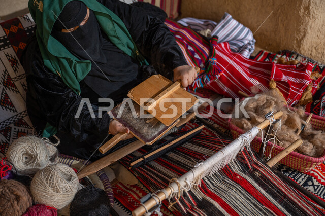 Preparing to weave and spin threads, preserving Saudi heritage, a historical profession and handicraft, the anniversary of the founding of the first Saudi state 1727 AD, a picture from above of a Saudi Gulf Arab woman wearing a black abaya and burqa combing wool, the day we started, February 22