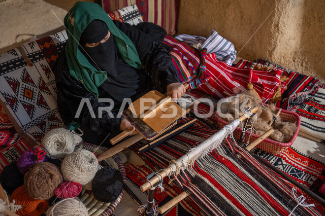 يوم بدينا 22 فبراير, الاستعداد لنسج وغزل الخيوط, المحافظة على التراث السعودي، مهنة وحرفة يدوية تاريخيه, ذكرى تأسيس الدولة السعودية الأولى 1727م, صورة من الاعلى لسيدة عربيه خليجية سعودية ترتدي العباءه السوداء و البرقع تقوم بتمشيط الصوف
