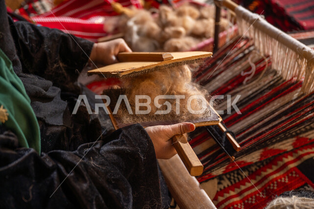 حرفة و مهنه يدوية تاريخيه, المحافظة على التراث السعودي، الاستعداد لنسج وغزل الخيوط, ذكرى تأسيس الدولة السعودية الأولى 1727م, صورة مقربة لسيدة عربيه خليجية سعودية ترتدي العباءه السوداء تقوم بتمشيط الصوف، يوم بدينا 22 فبراير