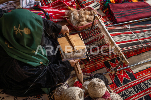 الاستعداد لنسج وغزل الخيوط, ذكرى تأسيس الدولة السعودية الأولى 1727م, يوم بدينا 22 فبراير, حرفة و مهنه يدوية تاريخيه, المحافظة على التراث السعودي، صورة من الاعلى لسيدة عربيه خليجية سعودية ترتدي العباءه السوداء و البرقع تقوم بتمشيط الصوف