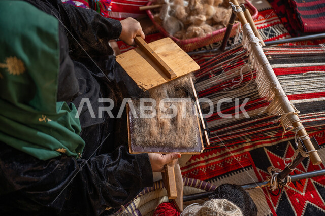 الاستعداد لنسج وغزل الخيوط, ذكرى تأسيس الدولة السعودية الأولى 1727م, يوم بدينا 22 فبراير, حرفة و مهنه يدوية تاريخيه, المحافظة على التراث السعودي، صورة من الاعلى لسيدة عربيه خليجية سعودية ترتدي العباءه السوداء و البرقع تقوم بتمشيط الصوف