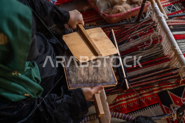 Preserving Saudi heritage, preparing to weave and spin threads, the anniversary of the founding of the first Saudi state 1727 AD, the day we started February 22, a historical handicraft and profession, a close-up image from above of a Saudi Arabian Gulf woman wearing a black abaya and burqa combing wool