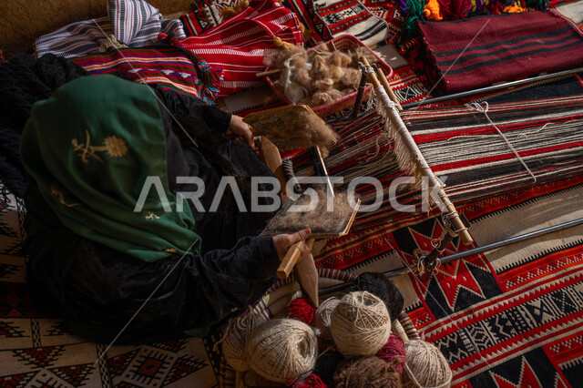 ذكرى تأسيس الدولة السعودية الأولى 1727م, مهنه و حرفة يدوية تاريخيه, الاستعداد لنسج وغزل الخيوط, يوم بدينا 22 فبراير, المحافظة على التراث السعودي، صورة من الاعلى لسيدة عربيه خليجية سعودية ترتدي العباءه السوداء و البرقع تقوم بتمشيط الصوف