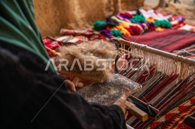 يوم بدينا 22 فبراير, ذكرى تأسيس الدولة السعودية الأولى 1727م, مهنه و حرفة يدوية تاريخيه, الاستعداد لنسج وغزل الخيوط, المحافظة على التراث السعودي، صورة مقربة لسيدة عربيه خليجية سعودية ترتدي العباءه السوداء تقوم بتمشيط الصوف