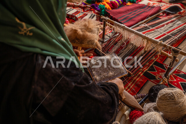 المحافظة على التراث السعودي، يوم بدينا 22 فبراير, ذكرى تأسيس الدولة السعودية الأولى 1727م, مهنه و حرفة يدوية تاريخيه, الاستعداد لنسج وغزل الخيوط, صورة مقربة لسيدة عربيه خليجية سعودية ترتدي العباءه السوداء تقوم بتمشيط الصوف